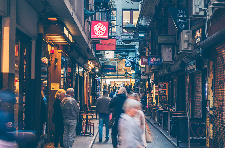 An alleyway in the city filled with cafe's, with many people walking through.